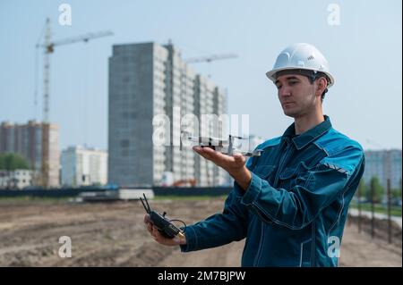 A man in a helmet and overalls controls a drone at a construction site. The builder carries out technical oversight. Stock Photo