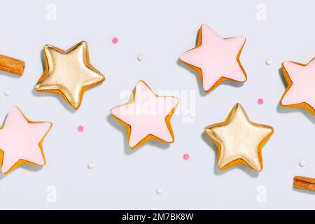 Holiday ginger cookies in the form of stars glazed sugar icing decoration on blue background with cinnamon sticks and topping for baking. Flat lay Stock Photo