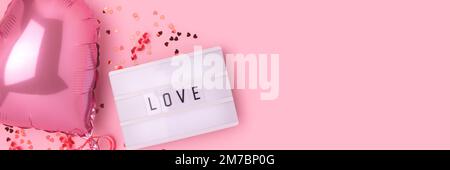 Word Love. Banner with lightbox, confetti and inflatable foil balloon in a heart shape on a pink pastel background. Selective focus. Stock Photo
