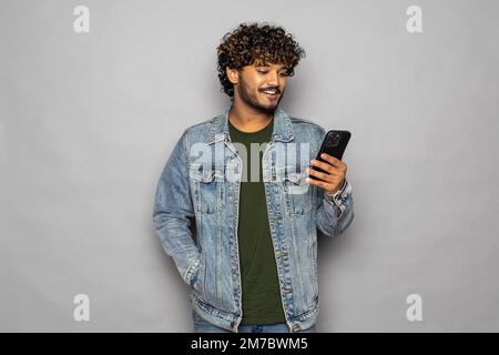 Excited indian business man using cell mobile phone isolated on gray background. Amazed ethnic guy holding smartphone feels surprised about betting wi Stock Photo