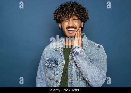 young bearded man wearing black T-shirt over blue studio background confuse and wonder about question. Uncertain with doubt, thinking with hand on hea Stock Photo