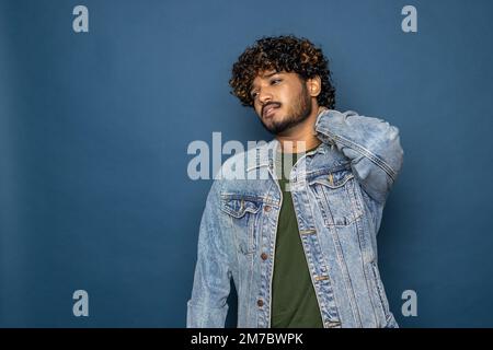 young bearded man wearing black T-shirt over blue studio background confuse and wonder about question. Uncertain with doubt, thinking with hand on hea Stock Photo