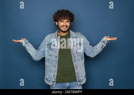 young bearded man wearing black T-shirt over blue studio background confuse and wonder about question. Uncertain with doubt, thinking with hand on hea Stock Photo
