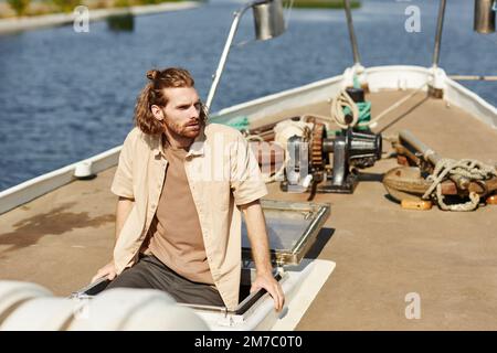 Portrait of bearded young man sailing on boat and looking away lit by sunlight, copy space Stock Photo