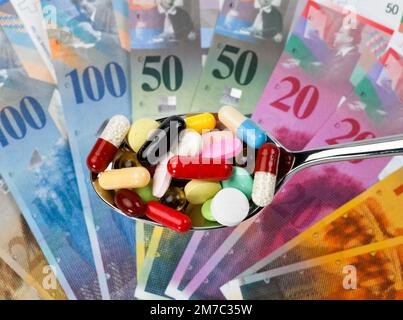colourful pills on a spoon against Swiss francs, cutout Stock Photo