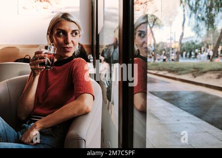 Woman looking out window while drinking a beverage in a restaurant. Stock Photo