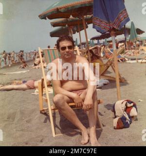 Man sitting in a reclioner on the beach, Italy 1960s Stock Photo