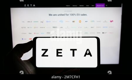 Person holding cellphone with logo of US Zero Emission Transportation Association (ZETA) on screen in front of webpage. Focus on phone display. Stock Photo