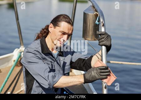 Side view portrait of smiling long haired sailor cleaning boat with care, scene lit by sunlight Stock Photo