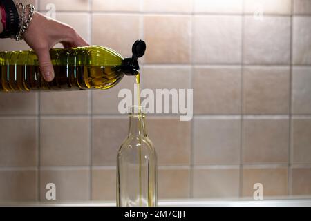 A stream of sparkling extra virgin olive oil, AOVE, as it pours from the plastic container into a glass bottle. Oil from the olive groves of Spain Stock Photo