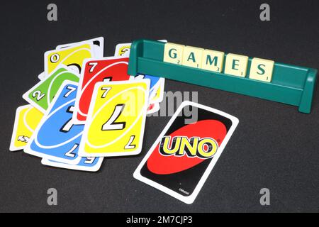 A games night concept showing scrabble tiles spelling out the word games on a reach and UNO cards spread out on an isolated black background Stock Photo