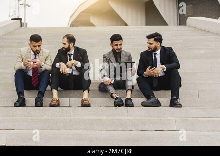 Business people outdoor meeting. A company of male businessmen in suits are sitting on the steps of the stairs. Working break. Discussion and Stock Photo