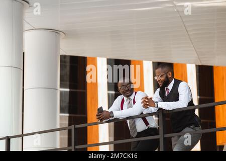 Portrait of two dark-skinned businessmen talking in the background of a modern building exterior. Friendly meeting outdoors Stock Photo