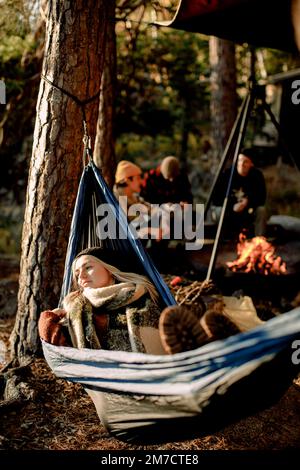 Young woman relaxing on hammock with friends camping in background Stock Photo