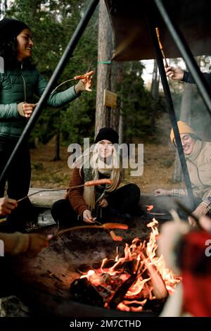 Happy male and friends enjoying food at campfire in forest Stock Photo