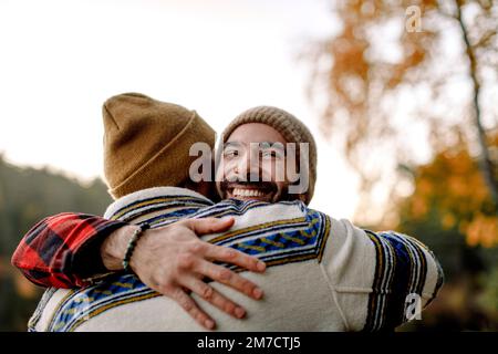 Young man embracing happy male friend wearing knit hat Stock Photo