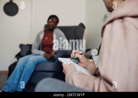 Non-binary counselor writing while discussing with female student in school office Stock Photo