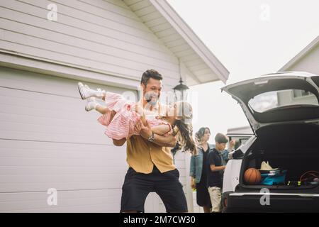 Happy father playing with daughter by electric car outside house Stock Photo
