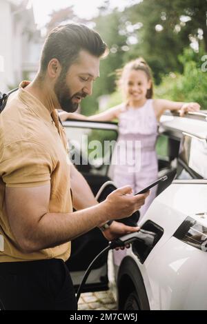 Side view of man using smart phone while charging electric car Stock Photo