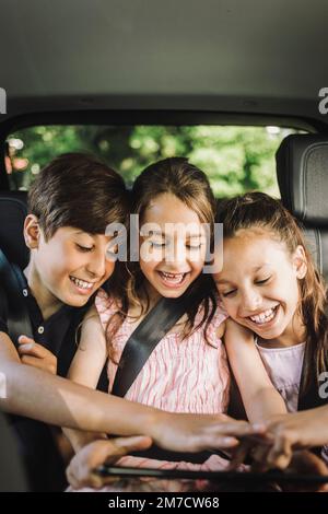 Happy siblings sharing tablet PC while while traveling in car Stock Photo