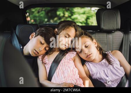 Tired siblings sleeping on back seat while traveling in car Stock Photo