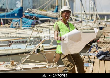 Portrait of black young woman looking at blueprints while working in yacht docks lit by sunlight, copy space Stock Photo