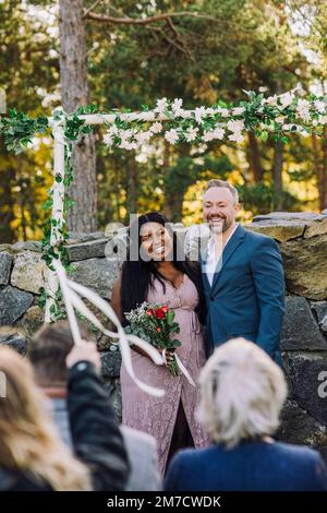 Happy bride standing with groom against wall looking at guests Stock Photo