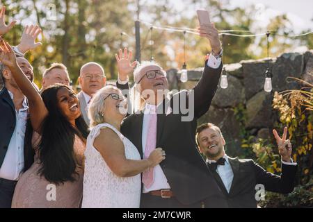 Happy newlywed senior couple taking selfie with family and friends through smart phone Stock Photo