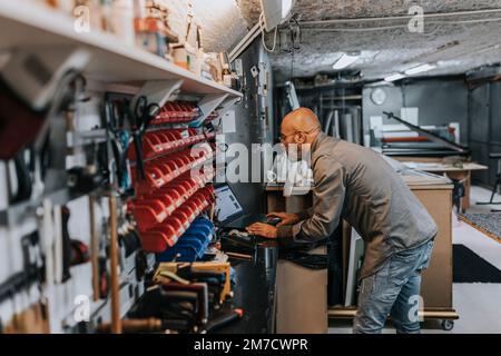 Bald male owner using laptop while working in workshop Stock Photo