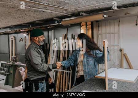Smiling young woman shaking hands with craftsman in workshop Stock Photo