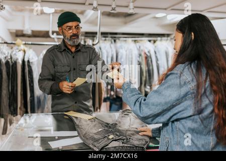 Young female customer giving bill to male tailor in workshop Stock Photo