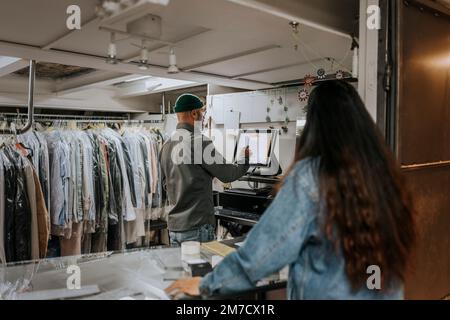 Rear view of young woman looking at male tailor using computer in workshop Stock Photo