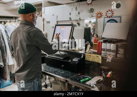 Rear view of male tailor using computer in workshop Stock Photo