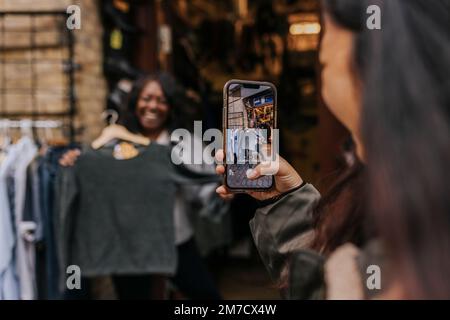 Young woman photographing female friend trying on clothes Stock Photo