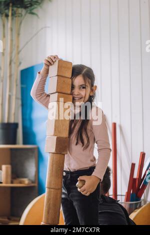 Smiling girl stacking wooden toy blocks in kindergarten Stock Photo