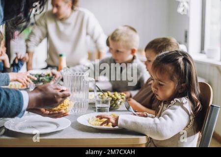 Teacher serving food to male and female students for breakfast in day care center Stock Photo