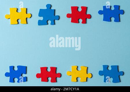 Blue, yellow, red pieces of puzzle on light blue frame background. World autism awareness day concept. Top view, copy space Stock Photo