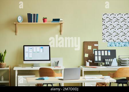 Background image of minimal office interior with computers on desks and pastel yellow wall, copy space Stock Photo