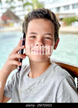 Close up portrait Happy teenage guy talking on mobile phone sitting on the beach Stock Photo