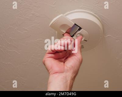 Replacing battery in home ceiling smoke detector fire alarm. Stock Photo