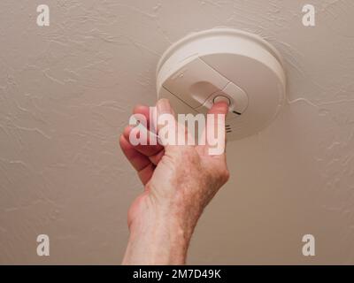Testing battery in home ceiling smoke detector fire alarm. Stock Photo
