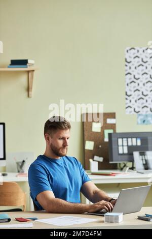 Vertical portrait of bearded young man using laptop while working at desk in minimal office setting Stock Photo