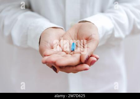 Women's hand with blue pill, vitamin, capsule. Medical insurance, medical treatment concept. Disease, sick treatment, cold season concept. Close-up vi Stock Photo