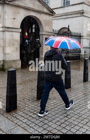 Person with patriotic Union Jack umbrella passing Horse Guards on Whitehall, Westminster, London, UK, in heavy rain. Visitor attraction in winter Stock Photo