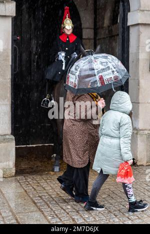 Visitors with patriotic umbrella passing Horse Guards on Whitehall, Westminster, London, UK, in heavy rain. Visitor attraction in winter. Child Stock Photo