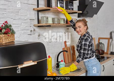 Woman in gloves cleaning furniture with rag at home kitchen. Stock Photo