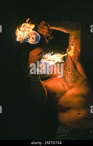 Fire dancer with body tattoo creating beautiful sparkling fire ball  on the beach at night Stock Photo