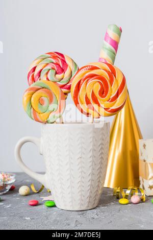 Colorful candies in cup on table on light background background. Large swirled lollipops. Creative concept of a jar full of delicious sweets from the Stock Photo