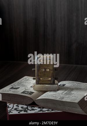 Old Antique Brass Desktop Perpetual Calendar Showing January 1th ( Vintage perpetual calendar ) placed on and old book with dark wooden background. We Stock Photo