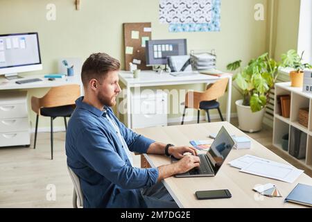 Side view portrait of bearded young man using laptop while working in cozy office, copy space Stock Photo